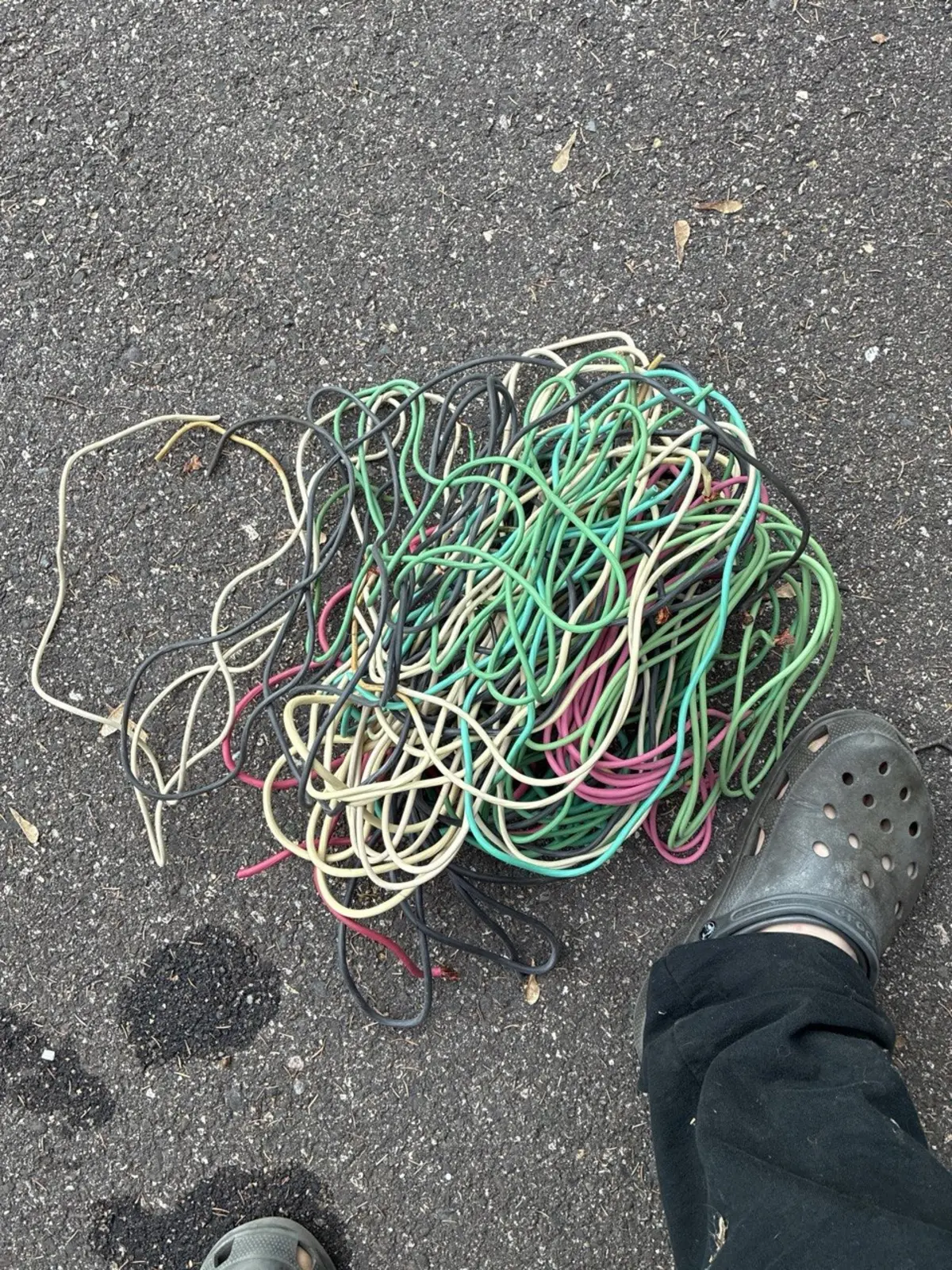 Pile of stripped bare bright copper on asphalt ready for scrap — green, cream, and pink wire insulation removed